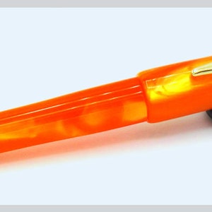 May include: Orange and white marbled fountain pen with a gold trim and a black pen rest.