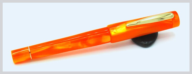 May include: Orange and white marbled fountain pen with a gold trim and a black pen rest.