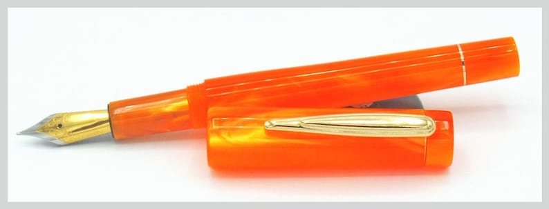 May include: A bright orange fountain pen with a gold-coloured nib and cap. The pen is made of a marbled acrylic material.