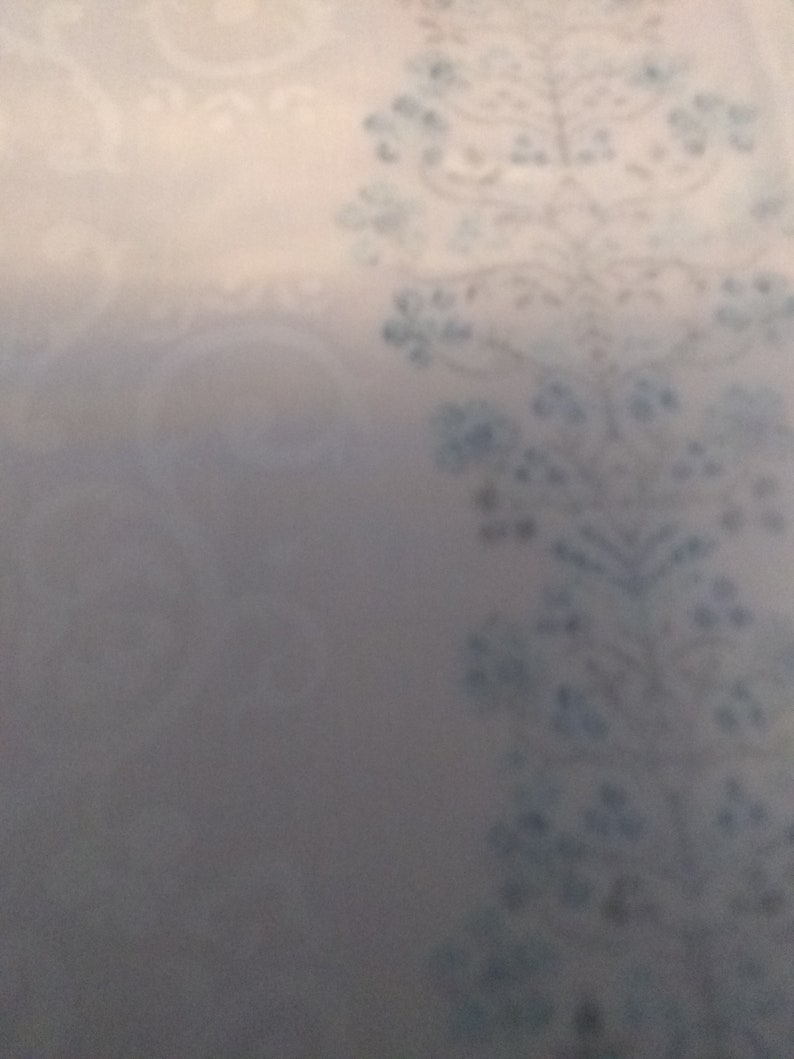 Columns of tiny blue flowers between white curling design on cream cotton polyester blend