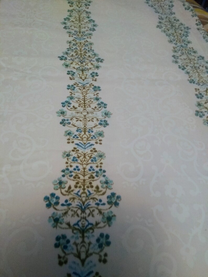 Columns of tiny blue flowers between white curling design on cream cotton polyester blend