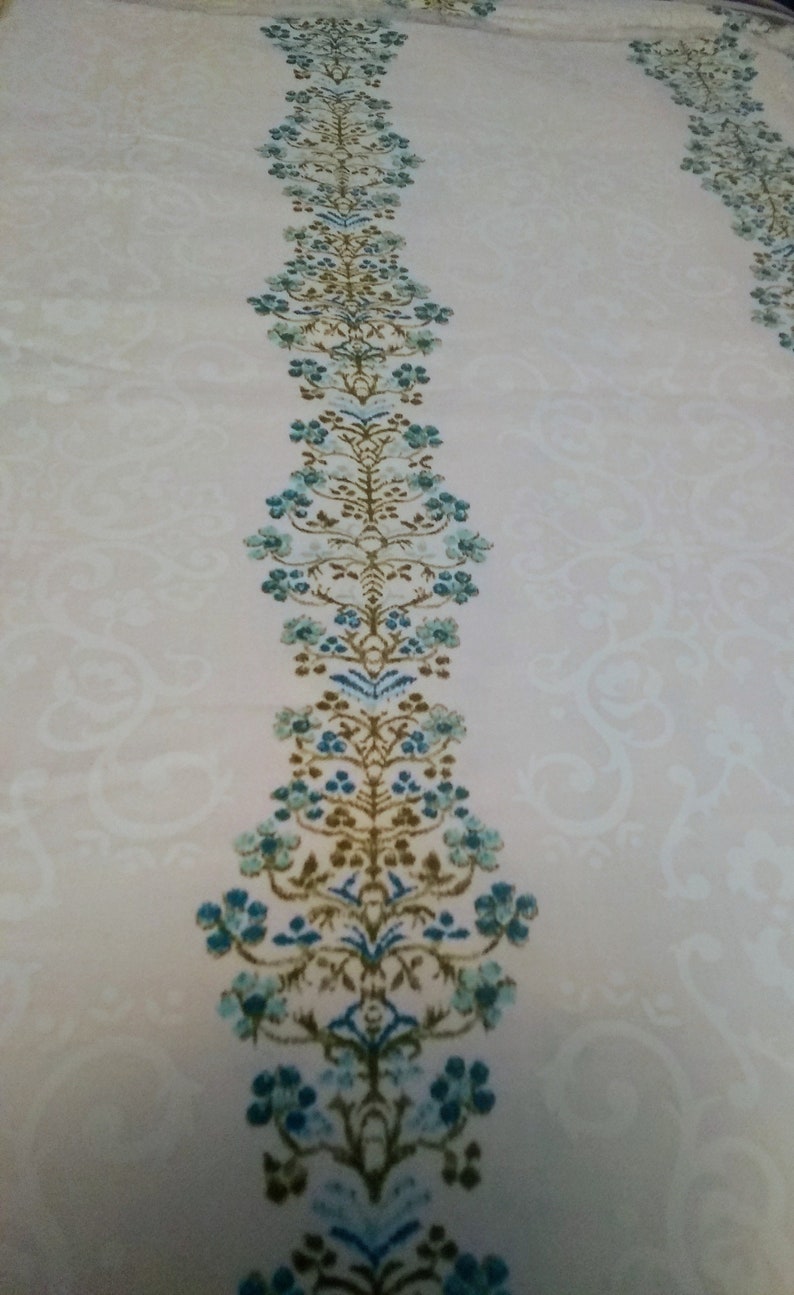 Columns of tiny blue flowers between white curling design on cream cotton polyester blend