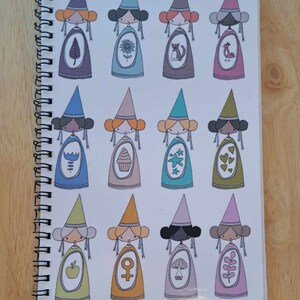 May include: A spiral bound notebook with a white cover featuring a repeating pattern of 12 illustrated figures wearing pointed hats. Each figure has a different coloured hat and dress, and a unique symbol or design on their dress.