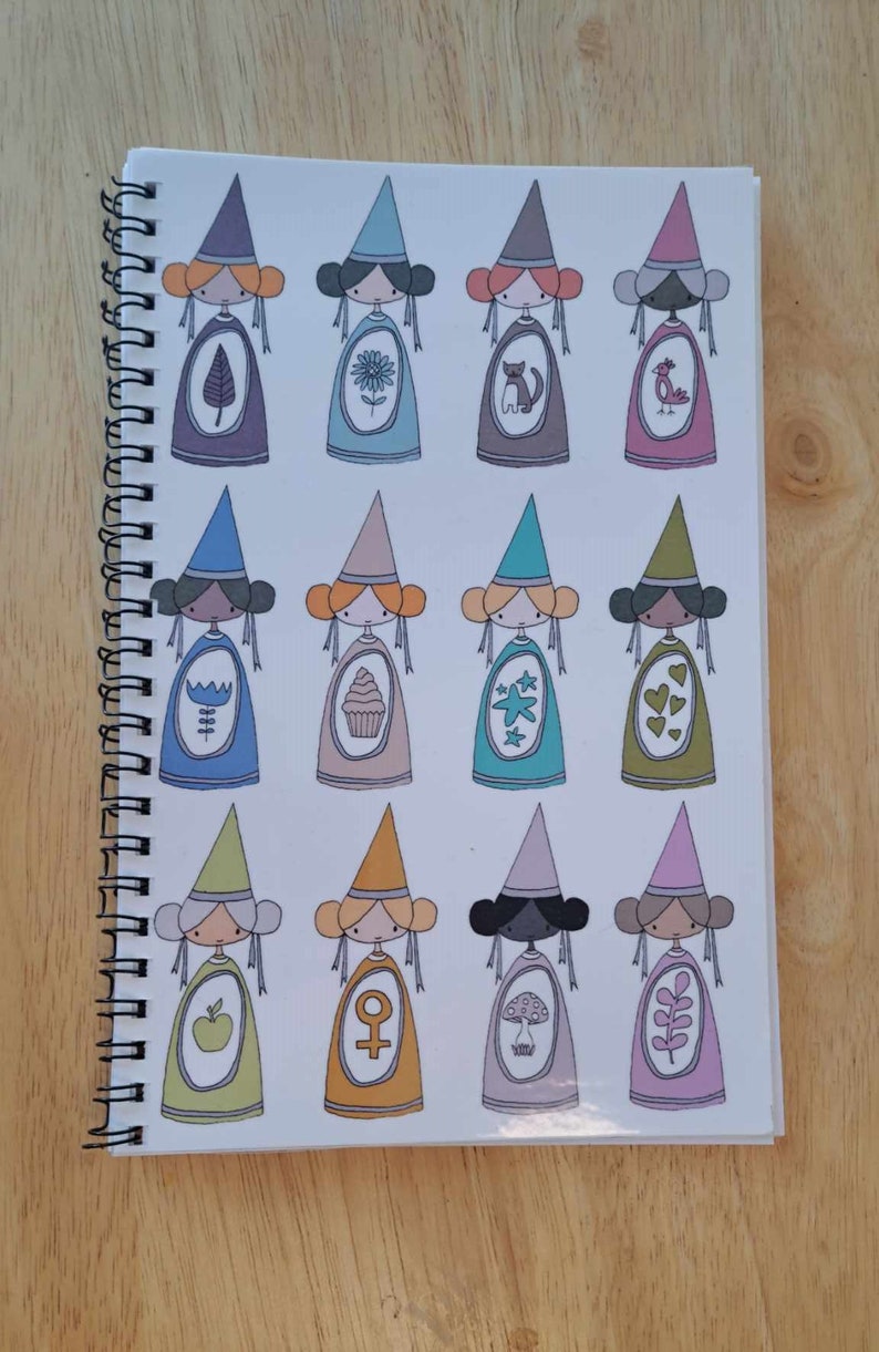 May include: A spiral bound notebook with a white cover featuring a repeating pattern of 12 illustrated figures wearing pointed hats. Each figure has a different coloured hat and dress, and a unique symbol or design on their dress.