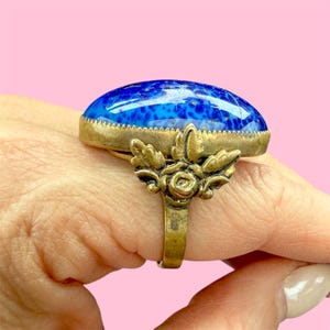May include: An antique brass ring with a large, oval, blue stone. The stone has a speckled pattern and is set in a brass bezel. The ring features a decorative floral design on the band.