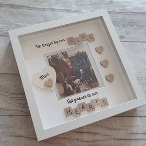 May include: White picture frame with a photo of a family. The frame has a white heart with the word "Max" on it. The frame also has wooden letter tiles spelling out "No longer by our side" and "But forever in our hearts".