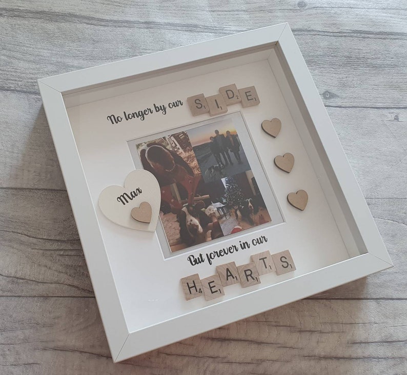 May include: White picture frame with a photo of a family. The frame has a white heart with the word "Max" on it. The frame also has wooden letter tiles spelling out "No longer by our side" and "But forever in our hearts".