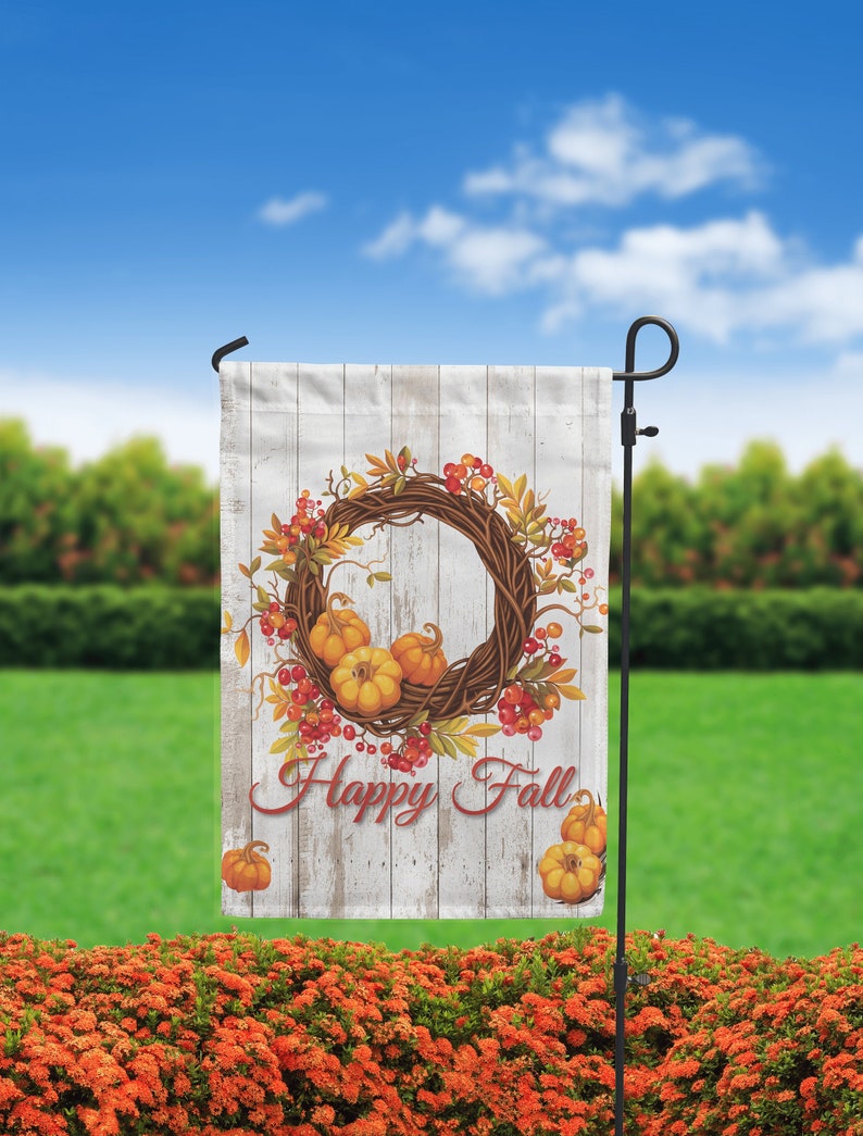 Puede incluir: Una bandera de jard&iacute;n con un dise&ntilde;o r&uacute;stico que presenta una corona de follaje oto&ntilde;al, calabazas y bayas. La bandera tiene un fondo de madera desgastada y las palabras "Happy Fall" en una fuente de escritura. La bandera se muestra en un soporte de metal negro.