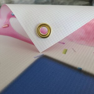 May include: Close-up of a white banner with a gold grommet. The banner is printed with a pink and white design with sprinkles.