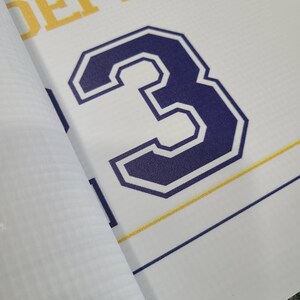 Op de afbeelding: Een witte banner met het woord "ACADEMY" in gele letters en het nummer "3" in een donkerblauwe omtrek met een witte binnenkant.