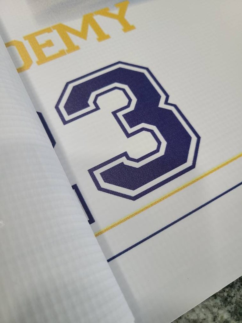 Op de afbeelding: Een witte banner met het woord "ACADEMY" in gele letters en het nummer "3" in een donkerblauwe omtrek met een witte binnenkant.
