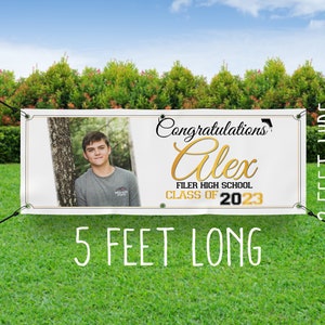 Op de afbeelding: Witte afstudeerbanner met een gouden en zwart ontwerp. De banner bevat een foto van een persoon, de tekst "Congratulations Alex", "Filer High School" en "Class of 2023". De banner is 1,5 meter lang en 0,6 meter breed.