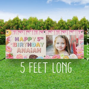 May include: A pink and white birthday banner with a donut theme. The banner says "Happy 5th Birthday Anaiah" and has a photo of a girl in the center. The banner is 5 feet long and 2 feet wide.