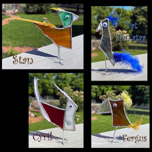 May include: Four stained glass bird sculptures with googly eyes and feathers. Stan is orange and green, Pat Hen'atar is grey and blue, Cyril is red and white, and Fergus is brown and yellow. Each bird stands on thin metal wire legs.