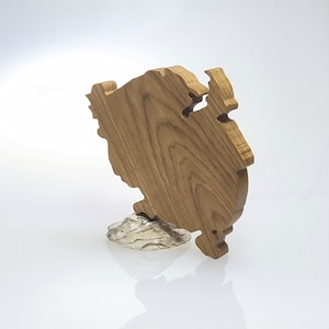 Könnte beinhalten: Ein Holzausschnitt einer stilisierten Insel mit einer natürlichen Holzoptik. Der Ausschnitt ist auf einem silbernen Metallsockel montiert.