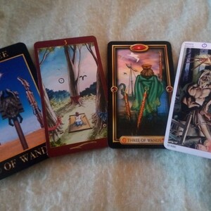 以下が含まれることがあります： 4枚のタロットカード。それぞれ異なる画像と番号が書かれています。カードは「ワンドの3」のカードです。最初のカードは、空に星が輝き、3本のワンドが描かれています。2枚目のカードは、木の前で座っている人が描かれています。3枚目のカードは、3本のワンドを持った人が船の上に立っている様子が描かれています。4枚目のカードは、3本のワンドを持った男性が椅子に座っている様子が描かれています。