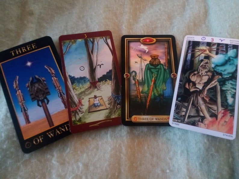 以下が含まれることがあります： 4枚のタロットカード。それぞれ異なる画像と番号が書かれています。カードは「ワンドの3」のカードです。最初のカードは、空に星が輝き、3本のワンドが描かれています。2枚目のカードは、木の前で座っている人が描かれています。3枚目のカードは、3本のワンドを持った人が船の上に立っている様子が描かれています。4枚目のカードは、3本のワンドを持った男性が椅子に座っている様子が描かれています。