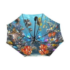May include: A colorful umbrella featuring a vibrant underwater scene. The design includes various fish, coral, and an octopus against a blue background. The umbrella has a black handle and frame, offering a whimsical and practical accessory.