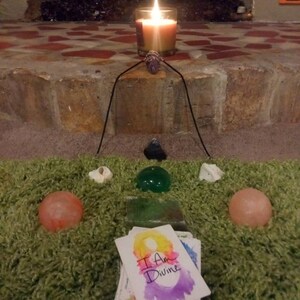 以下が含まれることがあります： 緑の敷物の上に、灯りがともったろうそく、クリスタル、そして「私は神聖である」と書かれたカードが置かれています。