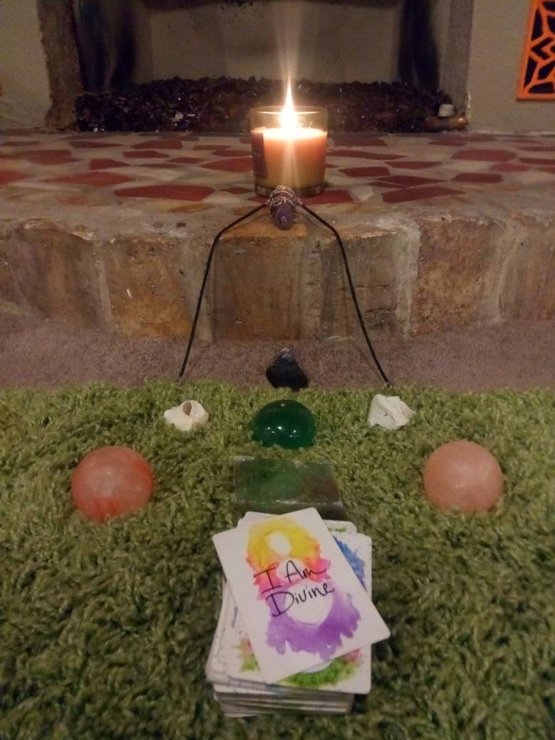 以下が含まれることがあります： 緑の敷物の上に、灯りがともったろうそく、クリスタル、そして「私は神聖である」と書かれたカードが置かれています。