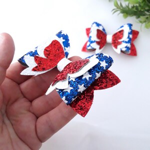 K&ouml;nnte beinhalten: Zwei rote, wei&szlig;e und blaue Glitzerb&ouml;gen mit einem Sternenmuster. Die Schleifen sind &uuml;bereinander gelegt und haben einen 3D-Effekt.