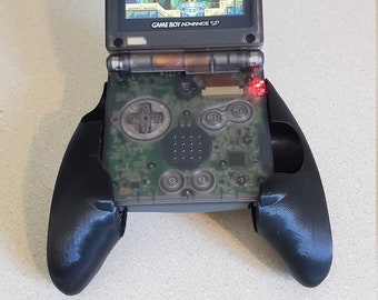 May include: A clear Game Boy Advance SP handheld gaming console with a black controller attachment. The console is displaying a video game on the screen. The text "GAME BOY ADVANCE SP" is visible on the console.
