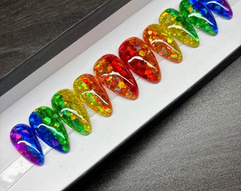 May include: A set of rainbow-colored, glitter-filled, almond-shaped false nails. The nails are arranged in a row inside a white box with a black border. The colors transition from purple to blue, green, yellow, orange, and red.