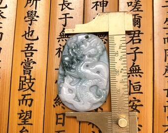 Peut inclure: Un pendentif en jade avec un motif de dragon sculpté. Le pendentif est vert et blanc et mesure environ 5 cm de long. Le pendentif est mesuré avec une règle.