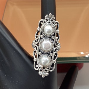 May include: A silver ring with three white pearls set in a decorative filigree design.