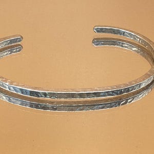 May include: A silver hammered bangle bracelet with a simple, minimalist design.