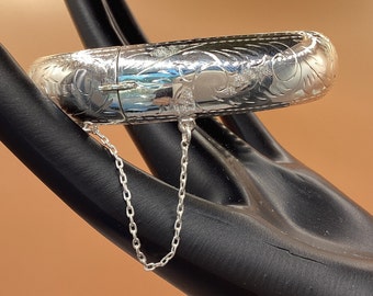 May include: A silver bangle bracelet with an engraved floral design and a chain attached to the clasp.