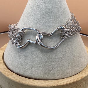 May include: A silver bracelet with two intertwined heart-shaped links and a chain-link design.