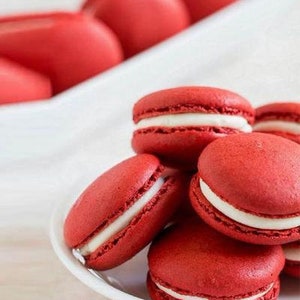 May include: A stack of red velvet macarons with white frosting. The macarons are arranged on a white plate.