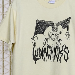May include: A vintage yellow t-shirt with a black graphic print of a winged demon and the text "Lunachicks".