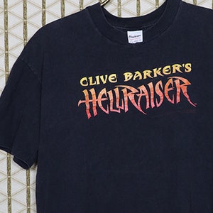 May include: A black t-shirt with a graphic print of "Clive Barker's Hellraiser" in orange and yellow lettering.