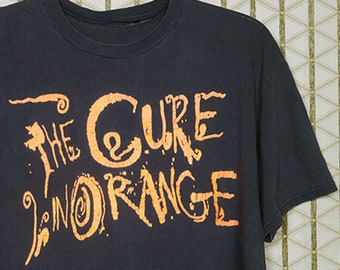 May include: A black t-shirt with an orange graphic print that reads "The Cure In Orange".