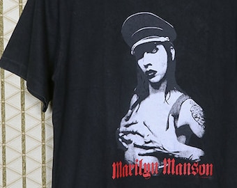 May include: Black t-shirt with a white and black image of Marilyn Manson wearing a military cap. The text "Marilyn Manson" is printed in red below the image.