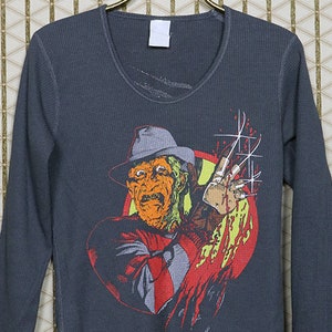 May include: A dark gray long-sleeved thermal shirt with a graphic print of Freddy Krueger from the movie "A Nightmare on Elm Street".