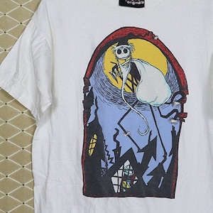 Puede incluir: Camiseta blanca con un estampado gr&aacute;fico de un personaje de dibujos animados de la pel&iacute;cula "Pesadilla antes de Navidad". El personaje est&aacute; de pie en un edificio con una luna llena en el fondo. El texto "Disney Originals" est&aacute; impreso en una etiqueta negra unida a la camiseta.