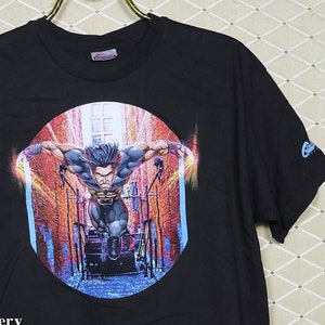 Puede incluir: Camiseta negra con un estampado gr&aacute;fico de un superh&eacute;roe en una escena de ciudad. El gr&aacute;fico est&aacute; en un marco circular con un esquema de color azul, rojo y naranja. El texto "CTMadrigal.com" est&aacute; impreso en la parte inferior de la camiseta.