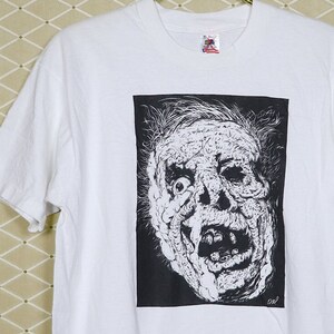May include: White t-shirt with a black and white illustration of a screaming face.