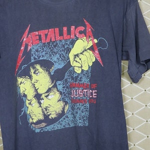 May include: A dark blue t-shirt with a graphic print of the band Metallica. The graphic features the band's name in red and black lettering and a multi-colored image of the band members. The text "...And Justice For All" is printed in yellow and red lettering.