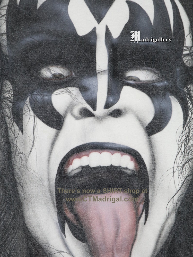 May include: A black and white illustration of a person with a demon-like face, with a large open mouth and tongue sticking out. The text "There's now a SHIRT shop at www.CTMadrigal.com" is visible at the bottom of the image. The text "Madrigalgallery" is visible in the top right corner of the image.