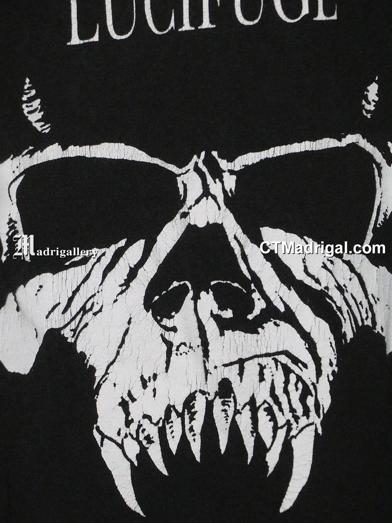 Puede incluir: Camiseta gr&aacute;fica en blanco y negro con un cr&aacute;neo con colmillos y la palabra "LUCIFUGE" impresa en la parte superior.
