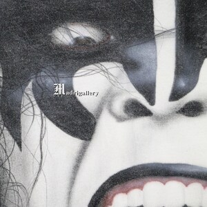 May include: A close-up black and white image of a person's face with a fierce expression. The person has long black hair and is wearing black makeup around the eyes. The mouth is open wide, revealing white teeth. The image is slightly grainy and has a vintage feel. There's now a SHIRT shop at www.CTMadrigal.com