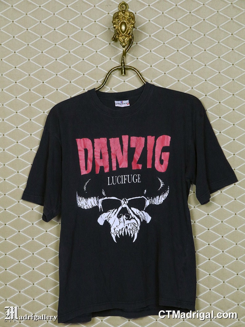 Puede incluir: Camiseta negra con un logotipo "Danzig" rosa y una calavera blanca con cuernos y el texto "Lucifuge" debajo.