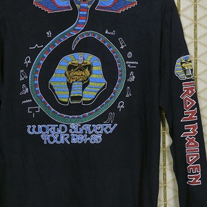 Pu&ograve; includere: Maglietta nera a maniche lunghe con una stampa grafica di un serpente, un faraone egizio e il testo "World Slavery Tour 1984-85". La manica destra ha il testo "Iron Maiden" stampato verticalmente.