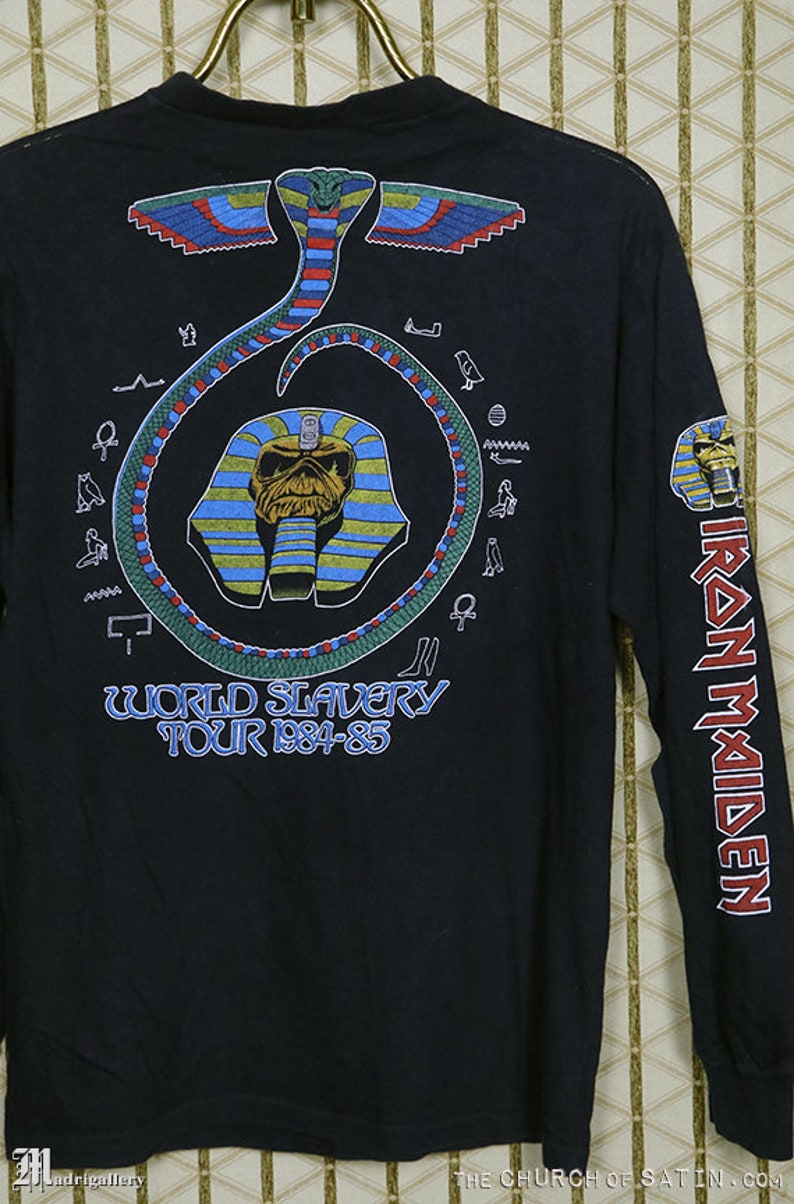 Pu&ograve; includere: Maglietta nera a maniche lunghe con una stampa grafica di un serpente, un faraone egizio e il testo "World Slavery Tour 1984-85". La manica destra ha il testo "Iron Maiden" stampato verticalmente.