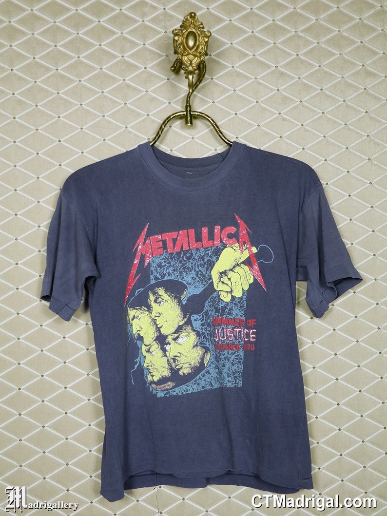 May include: A dark blue t-shirt with a graphic print of the band Metallica. The graphic features the band's name in red and black lettering and a multi-colored image of the band members. The text "...And Justice For All" is printed in yellow and red lettering.