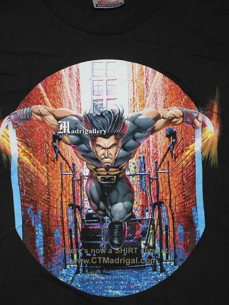 Puede incluir: Camiseta negra con un gr&aacute;fico circular de Wolverine, un superh&eacute;roe de Marvel Comics, corriendo por un callej&oacute;n de la ciudad. El gr&aacute;fico est&aacute; en un estilo vibrante y colorido con un esquema de color azul, rojo y amarillo. El texto "Madrigalley" y "www.CTMadrigal.com" son visibles en el gr&aacute;fico.